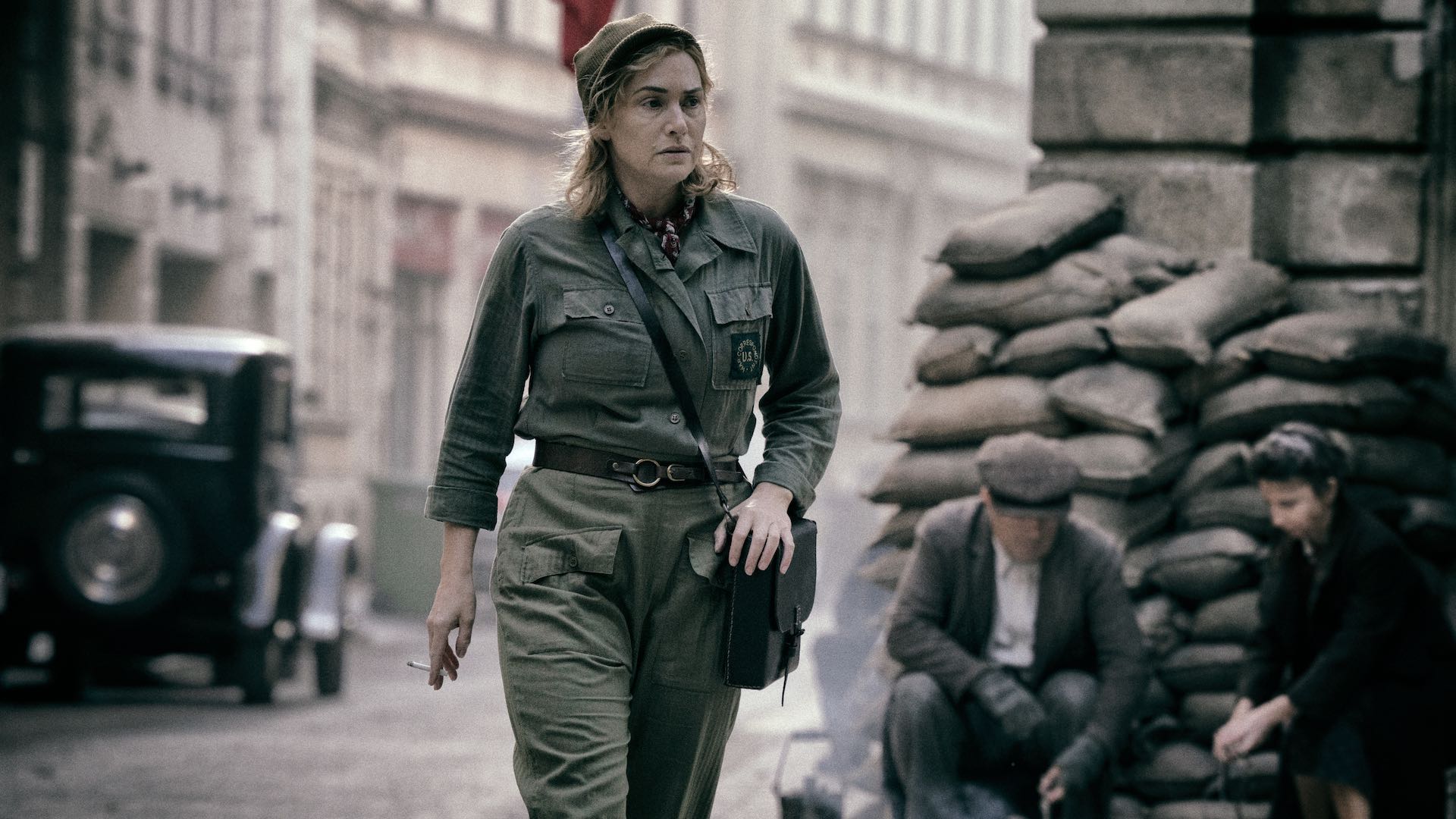 Kate Winslet as photographer Lee Miller in the film Lee (2023), walking through a sandbagged street.