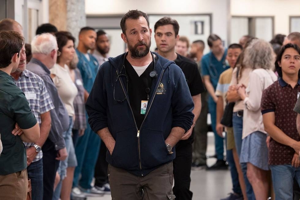 Noah Wyle in The Pitt, acting as a doctor walking in a hospital filled with people