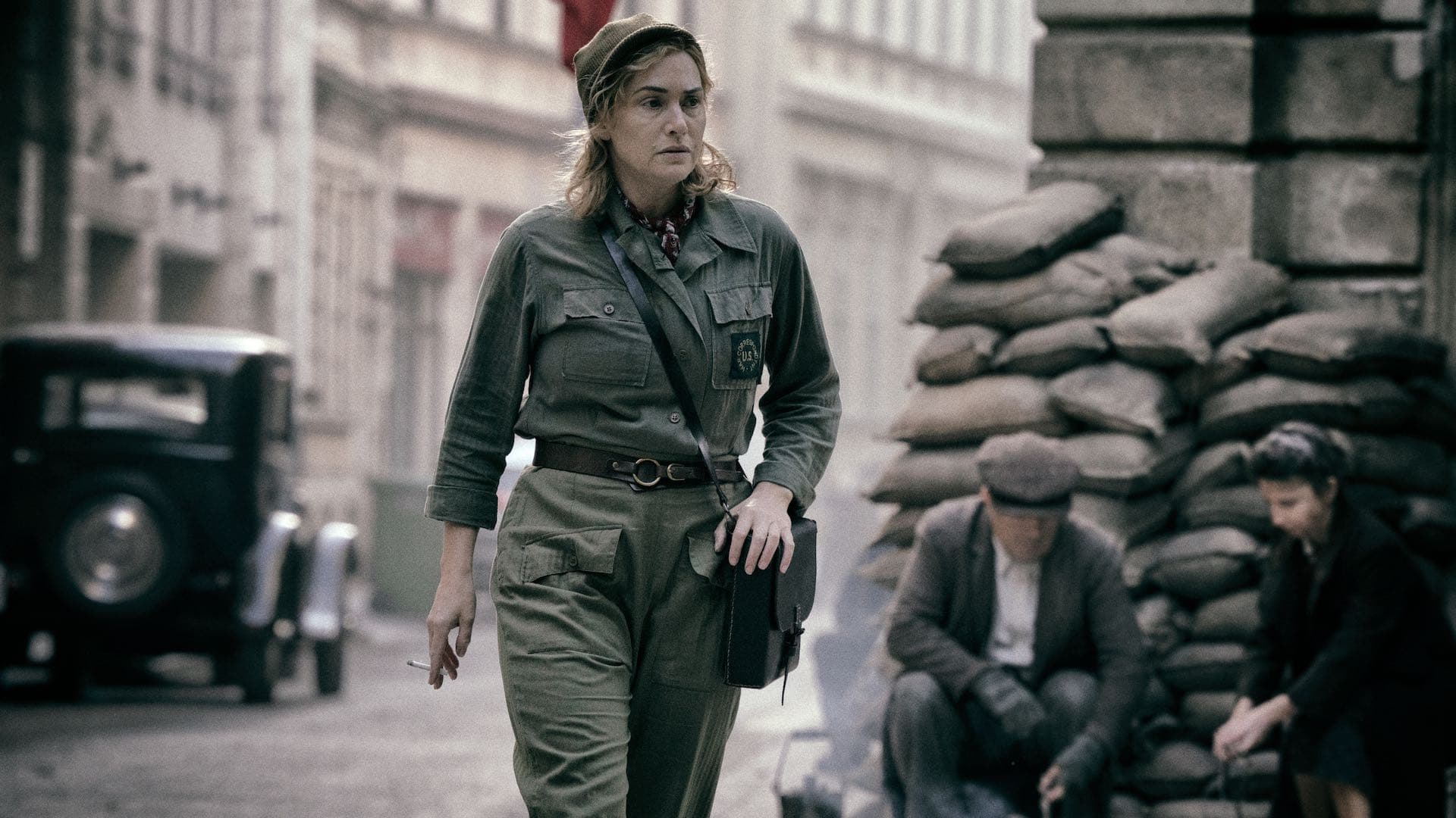 Kate Winslet as photographer Lee Miller in the film Lee (2023), walking through a sandbagged street.